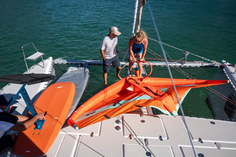 Two people assembling a kite surf on board a catamaran in harbour