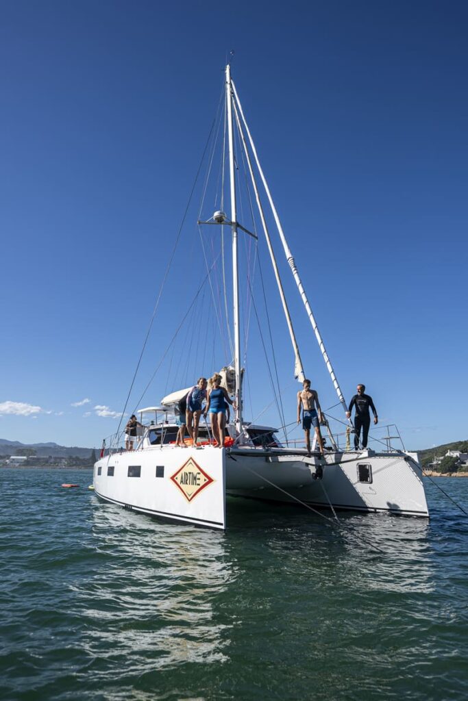 Catamaran with sails down anchored in still water with crew relaxing on deck